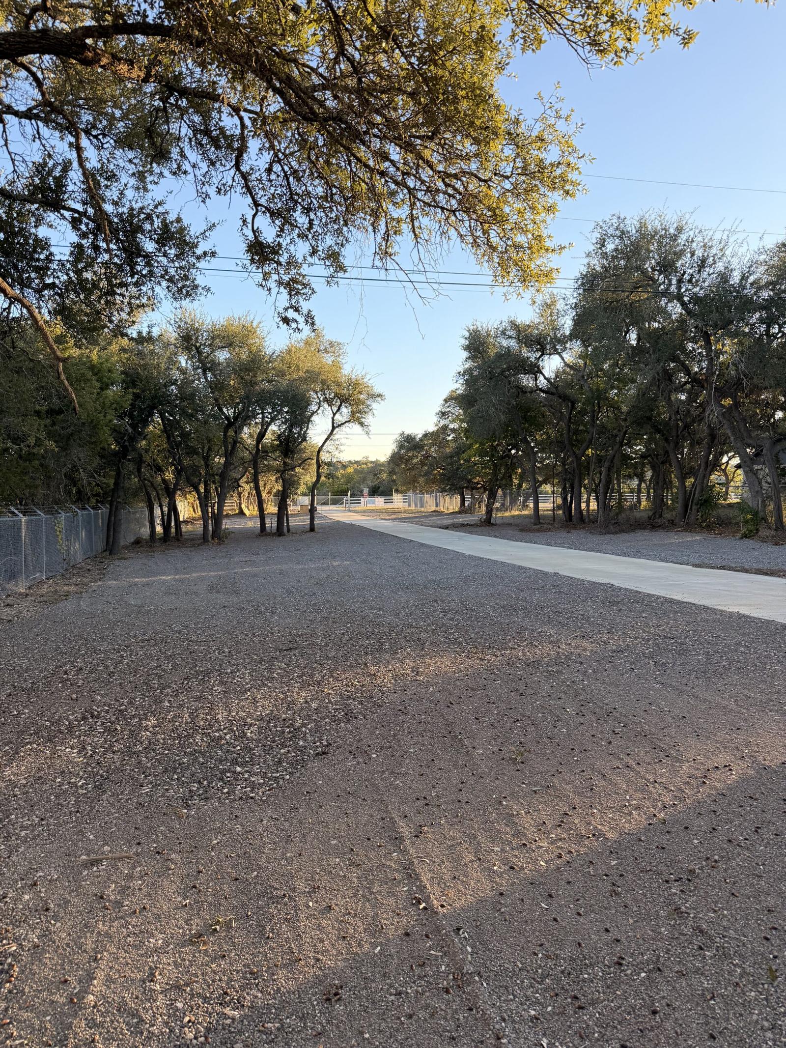 Tree-lined gravel entrance drive at Dripping Springs Self Storage