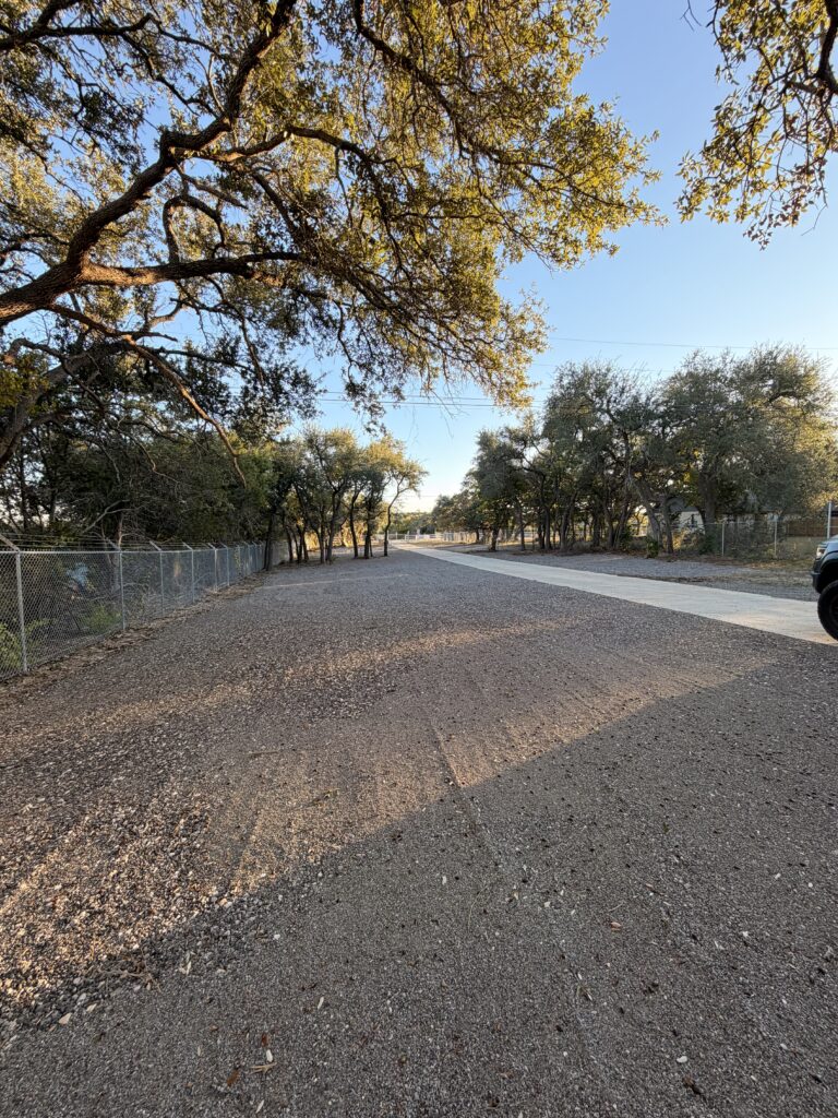 Tree-lined gravel entrance drive at Dripping Springs Self Storage